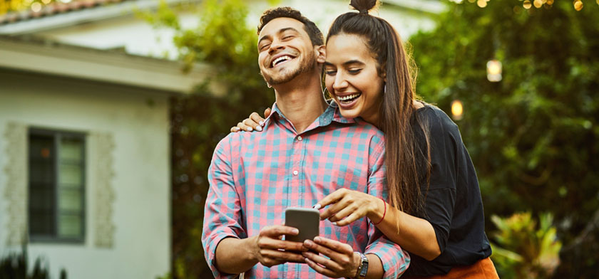 Man and woman outside of house looking at smart phone