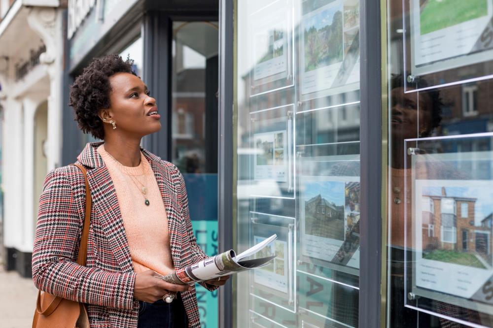 Woman looking at property listings outside real estate agent office